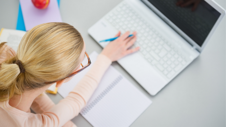 Woman working on a laptop with notebooks and an apple on the desk.